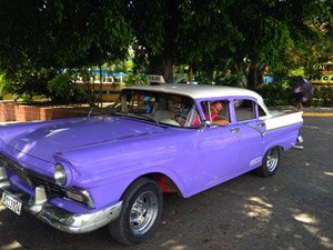 Lachende man bestuurt een paarse en witte vintage taxi in Cuba