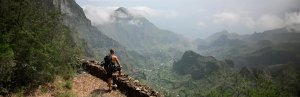 Wandelaar met rugzak kijkt uit over een weelderige groene bergvallei met wolken rond de bergtoppen in een bergachtig natuurgebied