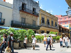 Zonnige voetgangersstraat in een historische stad met oude stenen en kleurrijke gebouwen, potplanten en mensen die rondlopen in Cuba