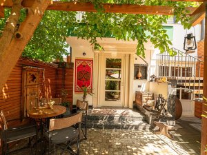 Sfeervol buitenterras in Kosovo met tafel en stoelen, rood wandkleed, wenteltrap en schaduw van een begroeide pergola