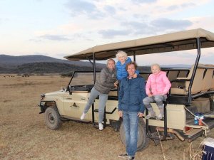 Gezin van vier poseert bij een safarivoertuig in een droog, open landschap in Zuid-Afrika