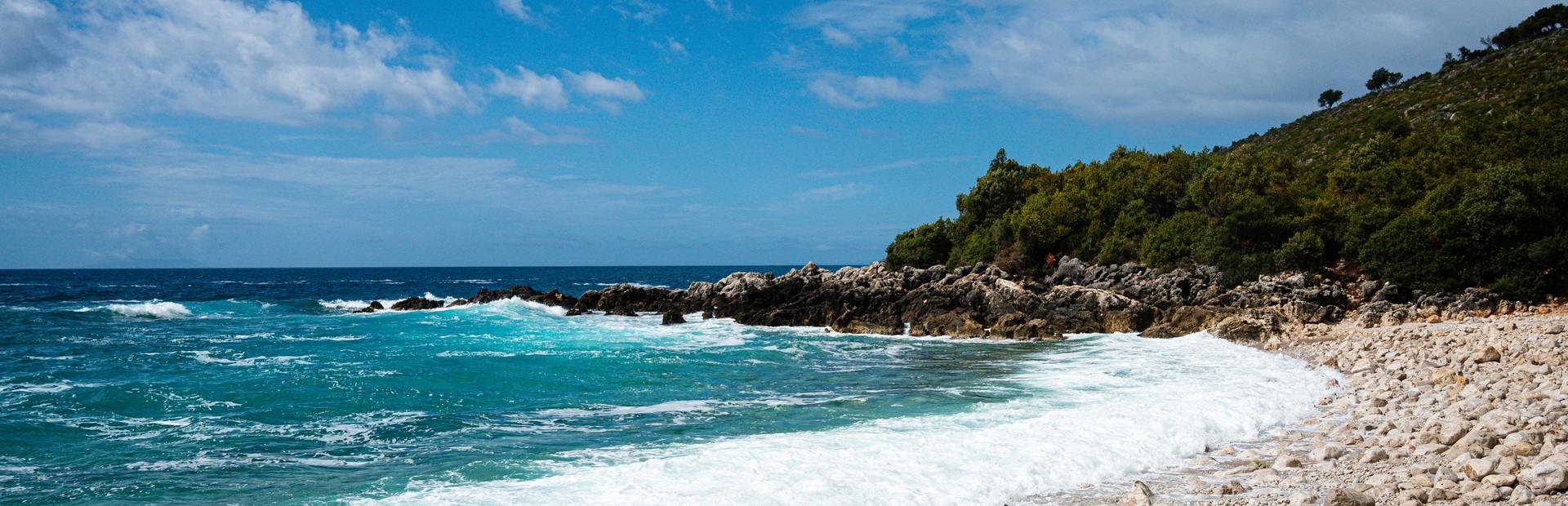 Panoramisch kiezelstrand Albanië turquoise zee en rotskust met bomen