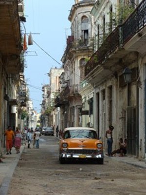 Vintage oranje-witte auto op een smalle versleten straat met vervallen gebouwen en voetgangers in Cuba