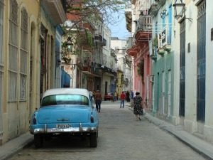 Lichtblauwe klassieke auto geparkeerd op een smalle straat met pastelkleurige gebouwen en voetgangers in Havana in Cuba