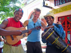 Drie glimlachende mannen, van wie er twee gitaar en drum spelen, poseren voor een foto in de buitenlucht in Cuba