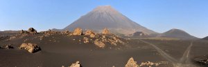 Panoramisch uitzicht op een kegelvormige vulkaan die uitsteekt boven een donkere rotsachtige vulkanische vlakte met een zandpad in een vulkanisch natuurgebied