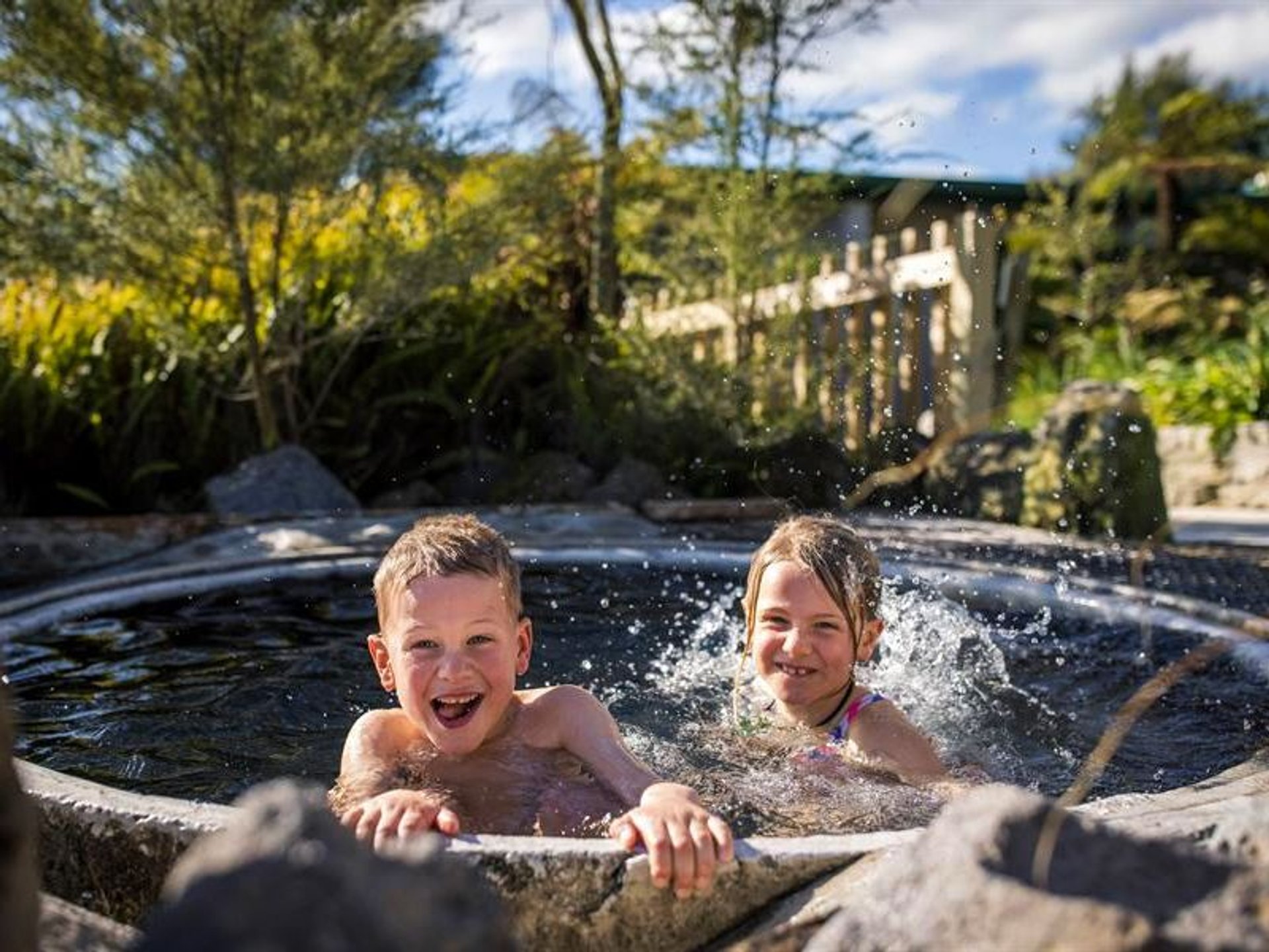 Twee kinderen lachen en spetteren met water in een buitenzwembad bij een vakantieverblijf