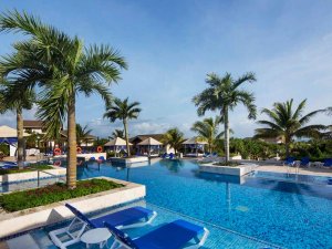 Tropisch resortzwembad met palmbomen, blauwe ligstoelen en cabana’s.