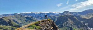 Persoon met gespreide armen staat op een rotsachtige top met uitzicht over een panoramische bergvallei en een gletsjer in de verte in IJsland
