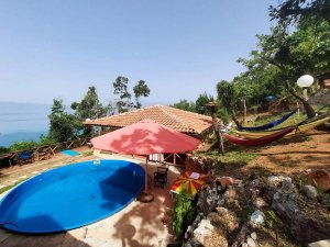 Resort op een zonnige heuvel in Albanië met een blauw ovaal zwembad, rode parasol en kleurrijke hangmatten met uitzicht op het water