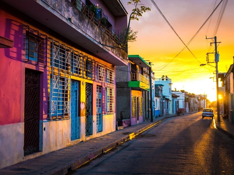 Kleurrijke straat in Cuba met levendige gebouwen en een auto onder een gouden zonsondergang