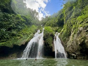 Een meerlagige waterval stort zich in een natuurlijk zwembad met zwemmers, omringd door dichte, groene jungle in Cuba