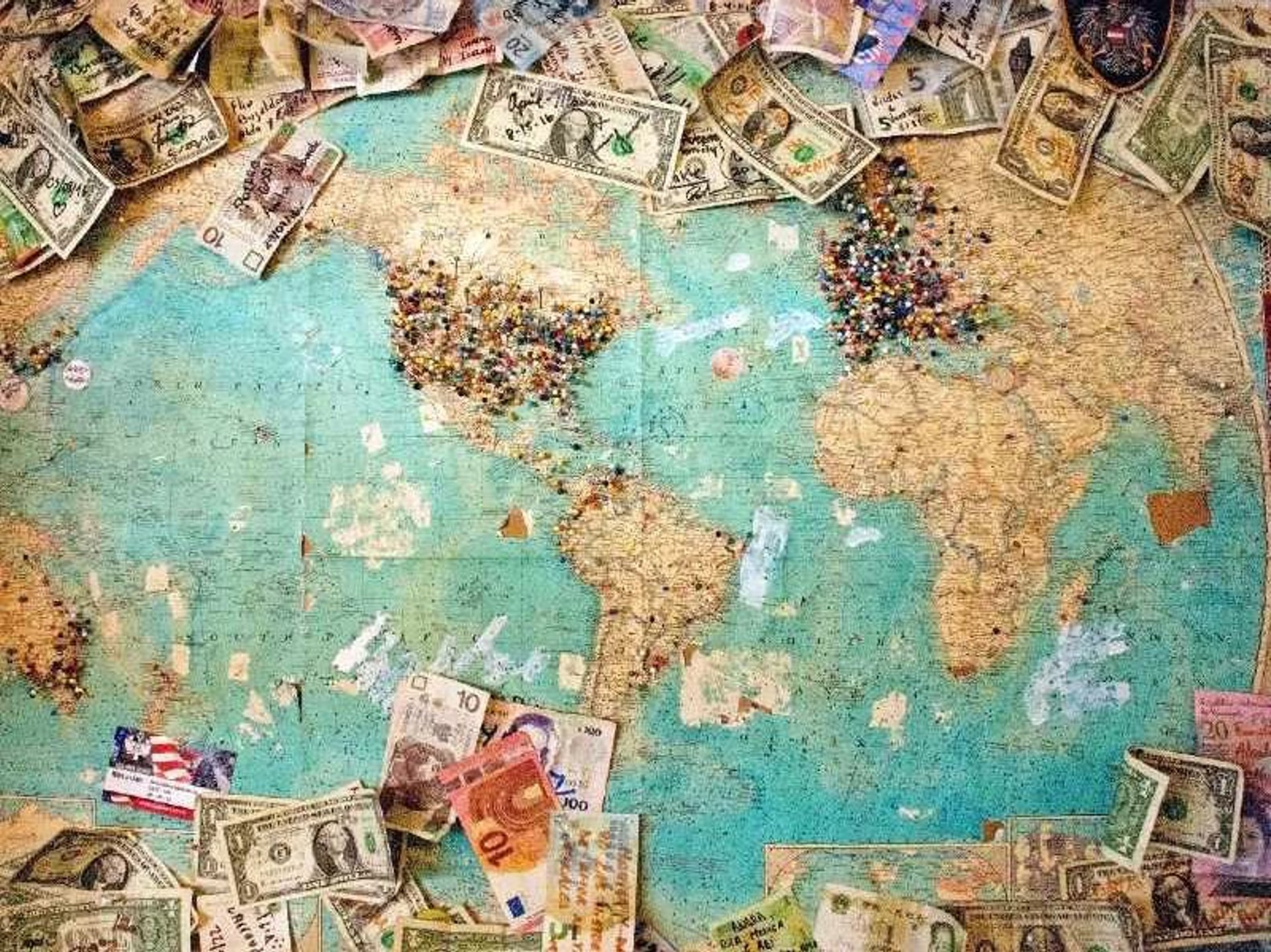 Vintage wereldkaart bedekt met internationale bankbiljetten en kleurrijke punaises in Nieuw-Zeeland