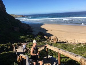 Vrouw en kind op houten traptreden boven een zandstrand, de oceaan en groene kliffen in Zuid-Afrika