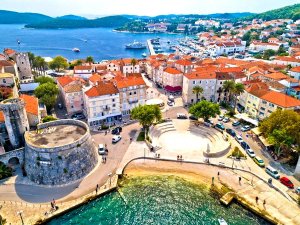 Luchtfoto van historische kuststad Korčula met rode daken, stenen fort, haven en amfitheater aan zee