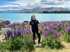 Lachende vrouw tussen paarse lupinebloemen bij een turquoise meer met bergen op de achtergrond in een bergachtig natuurgebied