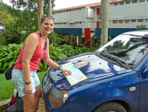 Lachende jonge vrouw die op de motorkap van een blauwe auto naar een kaart kijkt
