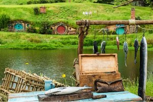Viskraam met hangende vissen naast een meer met hobbitwoningen in groene heuvels op de achtergrond in Nieuw-Zeeland