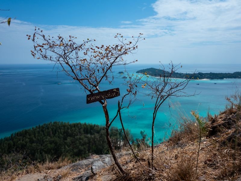 Uitzicht vanaf bergtop op turquoise zee en eilanden, met bordje ‘View Point 2’ aan een kale boom.
