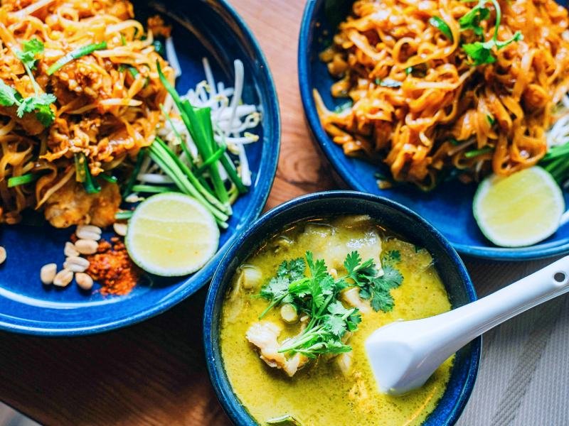 Drie borden met Thaise gerechten: curry en noedels met verse kruiden en limoen.