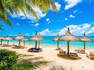 Tropisch strand met rieten parasols, ligstoelen, palmbomen en helderblauw water onder een deels bewolkte lucht in Zuid-Afrika