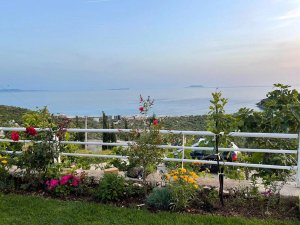 Uitzicht vanaf een tuin aan de Albanese Rivièra met bloemen, een hek en zicht op zee en de kustlijn