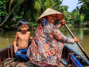 Vrouw peddelt over de Mekong met een brede glimlach