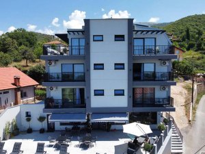 Modern grijs-wit gebouw in Albanië met meerdere verdiepingen, balkons en terras met ligstoelen tegen groene heuvels