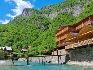 Houten guesthouses aan het Komanmeer in Albanië met een steiger en uitzicht op steile groene bergen