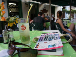 Mojito, zonnebril en Cuba reisgids op een groene terrastafel met mensen op de achtergrond in Havana in Cuba