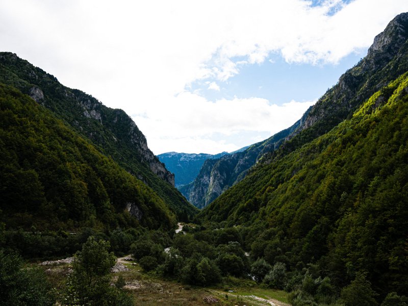Diepe vallei in Albanië met steile beboste bergen aan beide kanten onder een halfbewolkte lucht