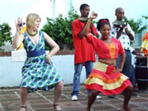 Blonde vrouw en donkere vrouw die samen dansen in Havana, Cuba met twee mannen op de achtergrond die pannen vasthouden