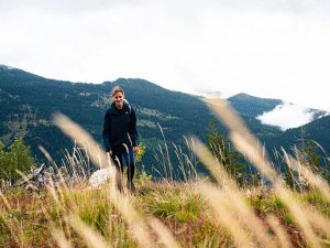 Vrouw wandelt door hoog gras in Rugova in Kosovo met uitzicht op groene bergen en mistige wolken