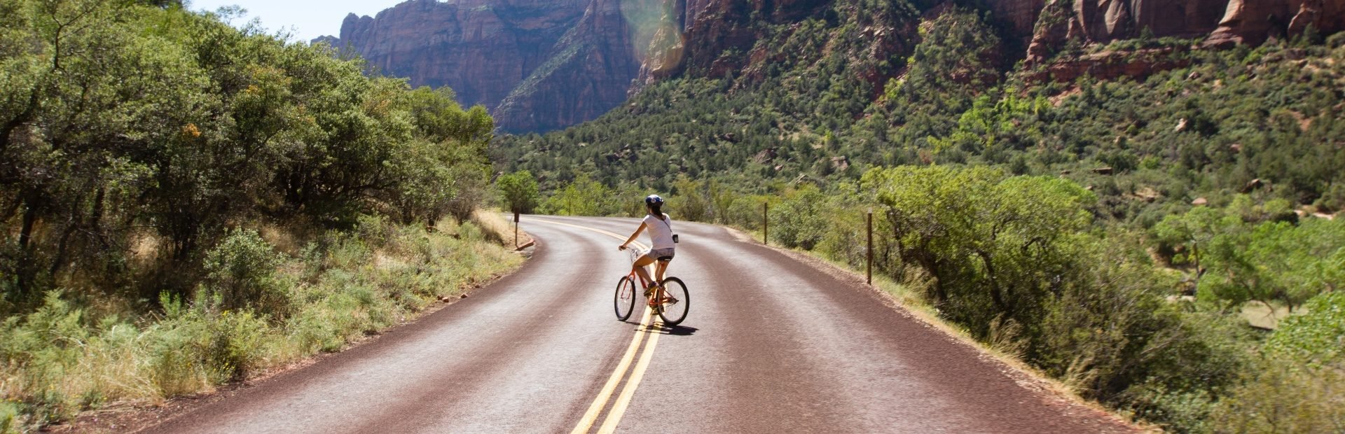 Fietser rijdt over een lege weg door een vallei met rode rotskliffen en groene begroeiing in Zion National Park, Verenigde Staten