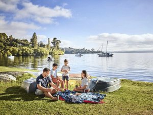 Gezin picknickt op een grasrijke oever van een meer met boten op het land en in het water in een natuurgebied