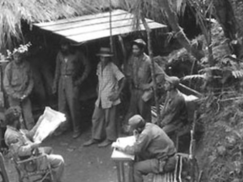 Mannen in een rustiek kamp in Cuba, terwijl één man een krant leest en een ander aan een tafel schrijft