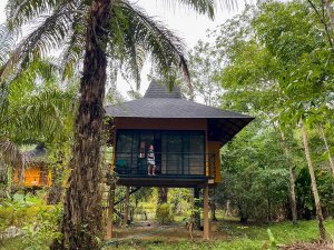 Een kindje wat op het balkon staat van een gele jungle lodge in de jungle van Khao Sok in Thailand met een palmboom op de voorgrond
