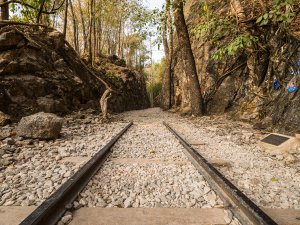 Oude treinrails lopen door een smalle doorgang tussen rotswanden en bomen in de jungle, onderdeel van de historische Dodenspoorlijn in Thailand.