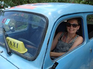 Lachende vrouw met zonnebril zit in een blauwe taxi in Cuba