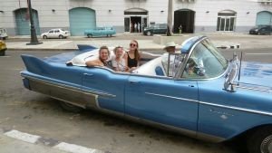 Vier mensen zitten in een blauwe vintage cabrio op een stadsstraat in Havana in Cuba