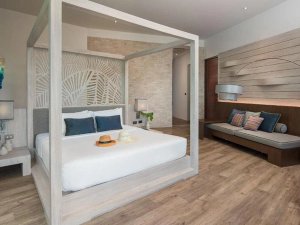 Modern ingerichte hotelkamer met hemelbed, houten vloer en een zithoek met gekleurde kussens.