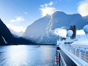 Cruiseschip vaart door een schilderachtige fjord met hoge bergen en een waterval in een bergachtig natuurgebied