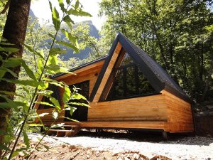 Moderne houten cabin aan het Komanmeer in Albanië midden in het bos met grote ramen en uitzicht op de bergen