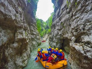 Groep mensen in een oranje raft met helmen en reddingsvesten peddelt door een smalle rotsachtige kloof tijdens raften in Osum Canyon, Berat, Albanië