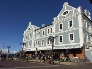 Lichtblauw gebouw met puntdak aan het water, met mensen op de voorgrond in Zuid-Afrika