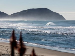 Zandstrand naast de oceaan met brekende golven en een opvallende krullende golf met mistige bergen in de verte aan de kust