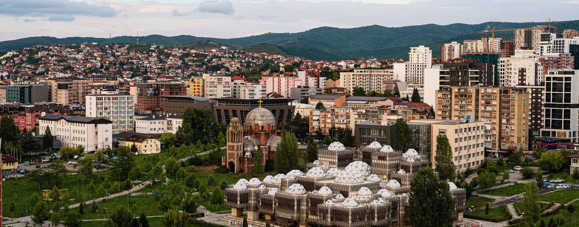 Panoramisch uitzicht op Pristina met de Nationale Bibliotheek van Kosovo en de Christus Verlosserkathedraal, omringd door stadsgebouwen en groene heuvels in Pristina in Kosovo