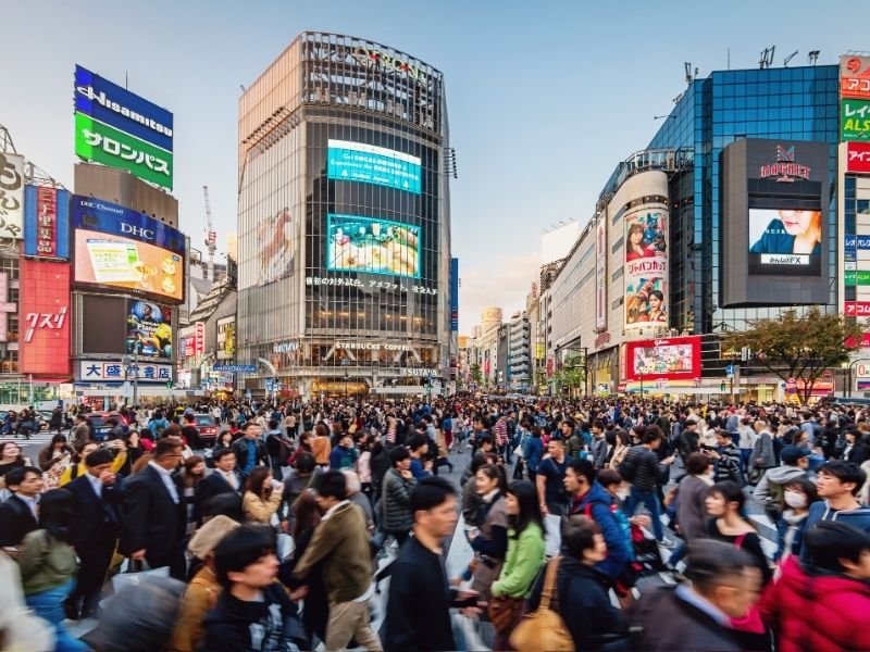 Drukke voetgangersoversteekplaats in Shibuya, Tokyo, Japan, omringd door hoge gebouwen met grote reclameborden.