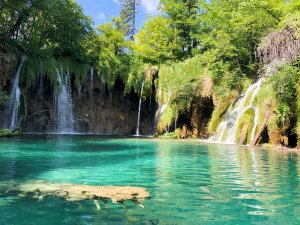 Meerdere watervallen stromen in een fel turquoise meer omringd door weelderig groen in Kroatië