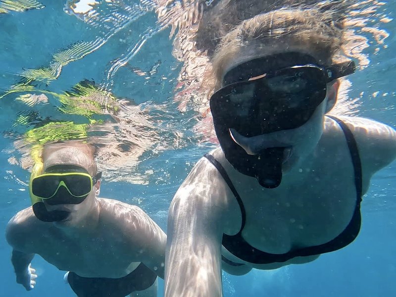 Twee reizigers maken een selfie terwijl ze onder water snorkelen met snorkelmaskers op. Het water om hen heen is helderblauw.